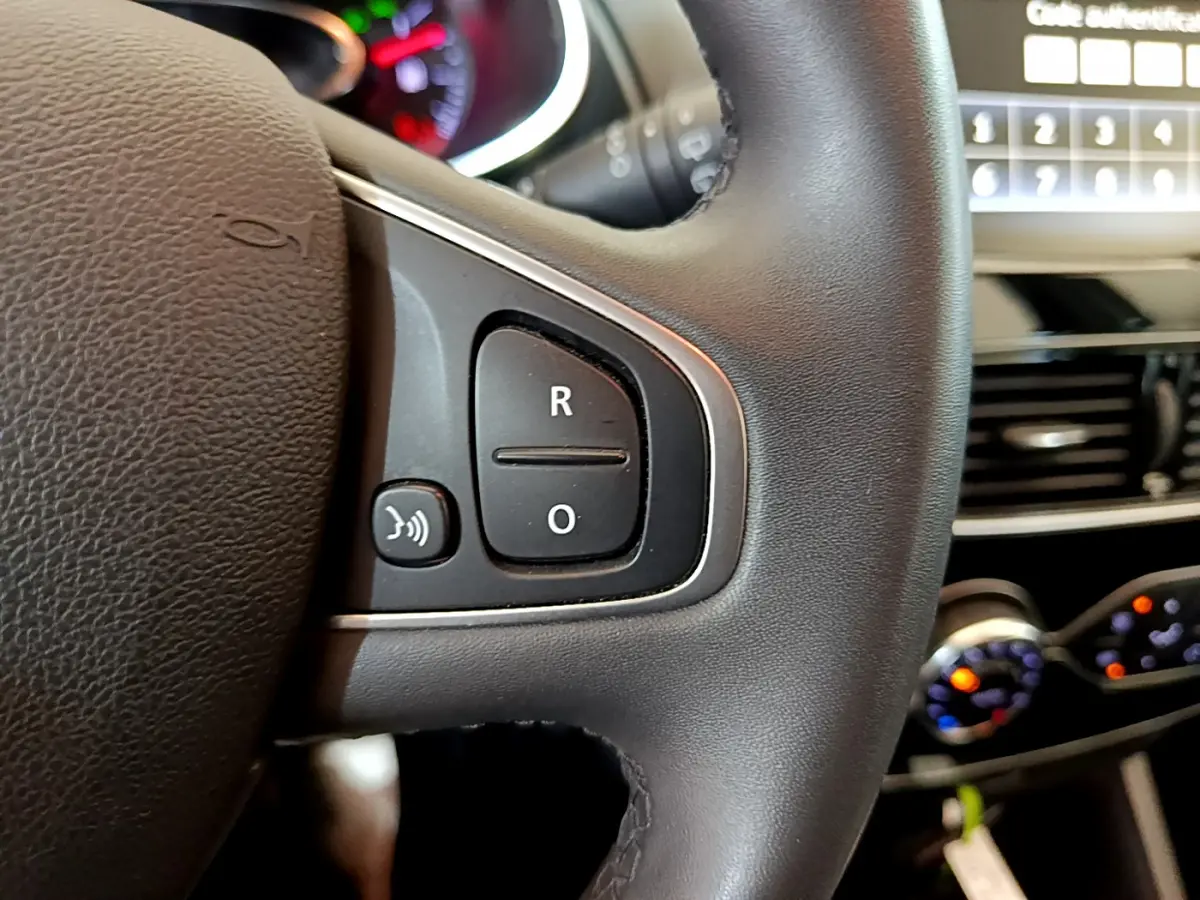 Gros plan sur les commandes du volant cuir noir de la Renault Clio Business TCe 90, avec tableau de bord et écran tactile en arrière-plan.