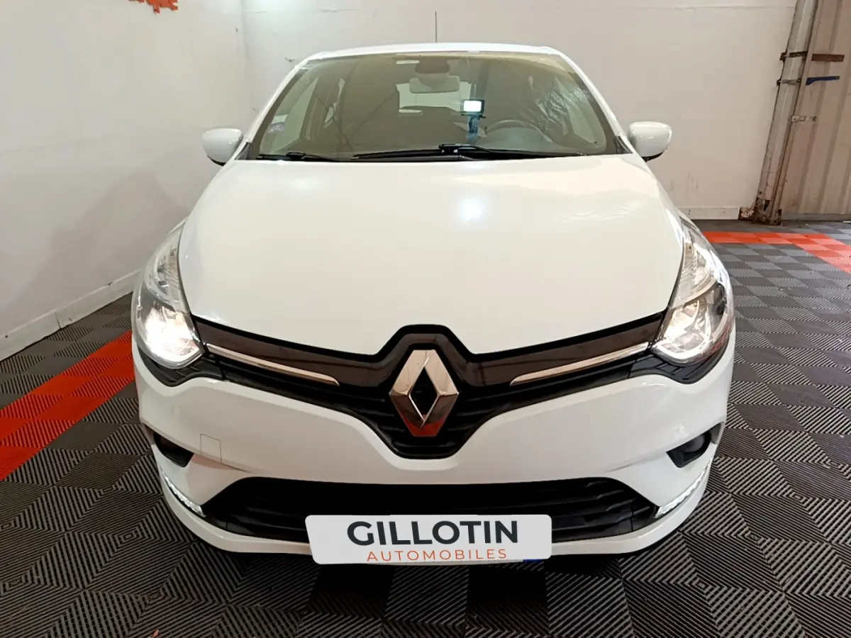 Vue frontale d'une Renault Clio Business TCe 90 blanche avec phares allumés et logo Renault bien visible.