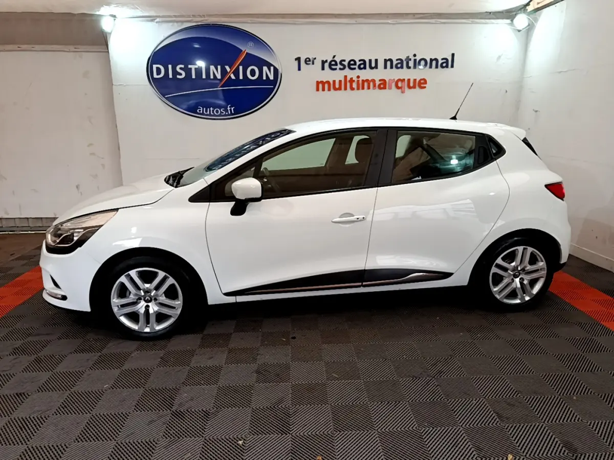 Profil droit d'une Renault Clio Business TCe 90 blanche, avec jantes alliage et logo Distinxion en arrière-plan.