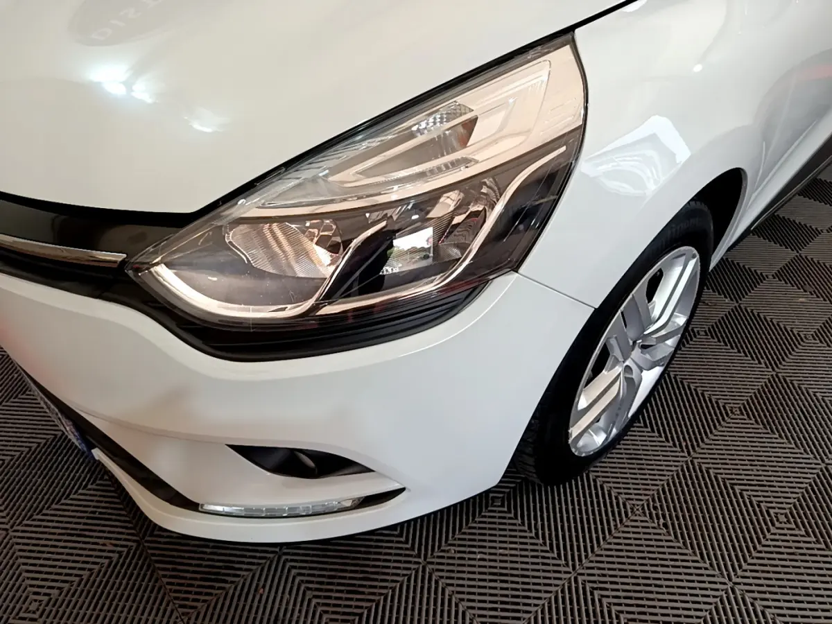 Gros plan sur le phare avant gauche et la roue d'une Renault Clio Business TCe 90 blanche de 2019.