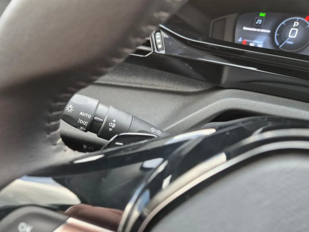 Vue rapprochée du volant et du commodo gauche de la Peugeot 308 2024, avec affichage numérique en arrière-plan.