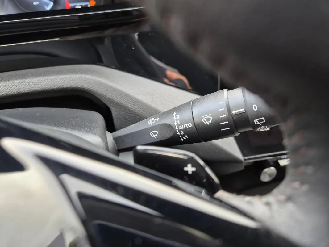Gros plan sur la commande des essuie-glaces côté gauche du volant dans l’habitacle d’une Peugeot 308 bleu 2024.