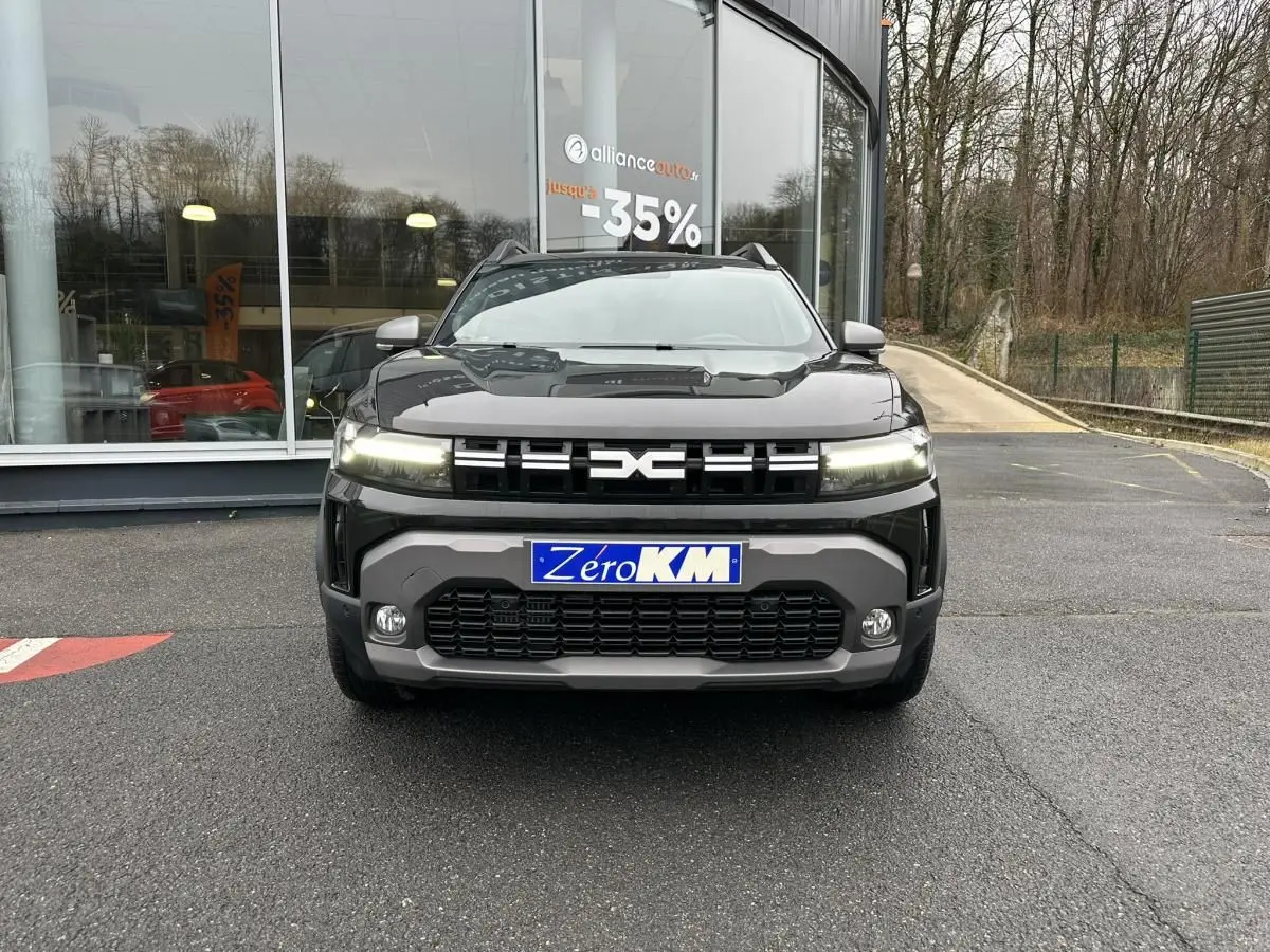 Vue frontale du Dacia Duster noir métallisé 2025 avec signature lumineuse LED et plaque Zéro KM visible.