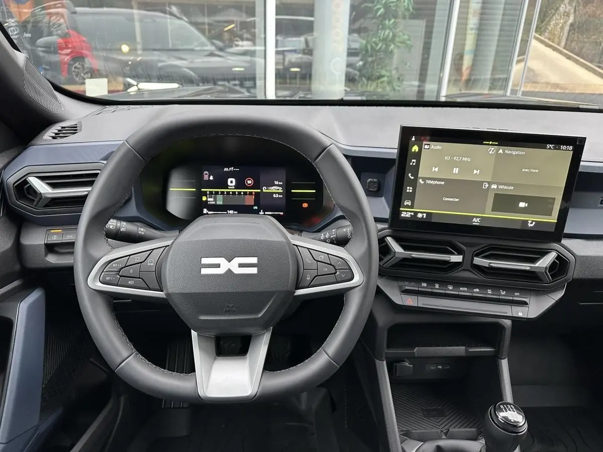 Vue intérieure frontale du tableau de bord noir du Dacia Duster 2025 avec volant multifonction et écran tactile central.