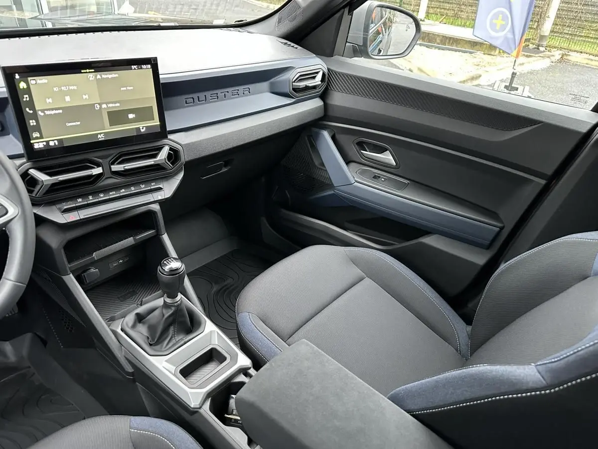 Intérieur du Dacia Duster 2025 vu côté passager, montrant la console centrale avec boîte manuelle et sièges noirs.