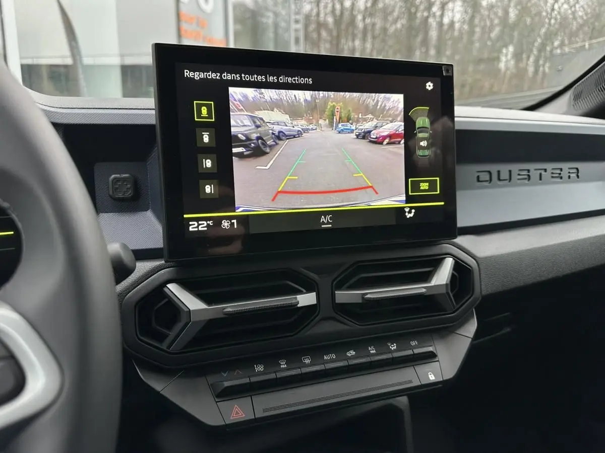 Vue intérieure du tableau de bord du Dacia Duster 2025 noir, avec écran de caméra de recul et aérateurs hexagonaux.