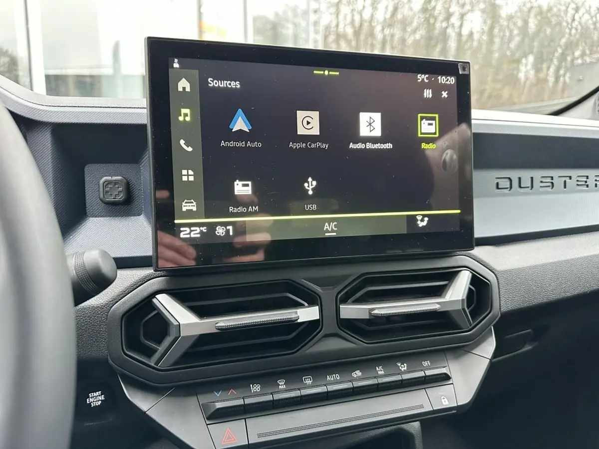 Vue intérieure du tableau de bord du Dacia Duster 2025 noir, avec écran tactile central et aérateurs hexagonaux.