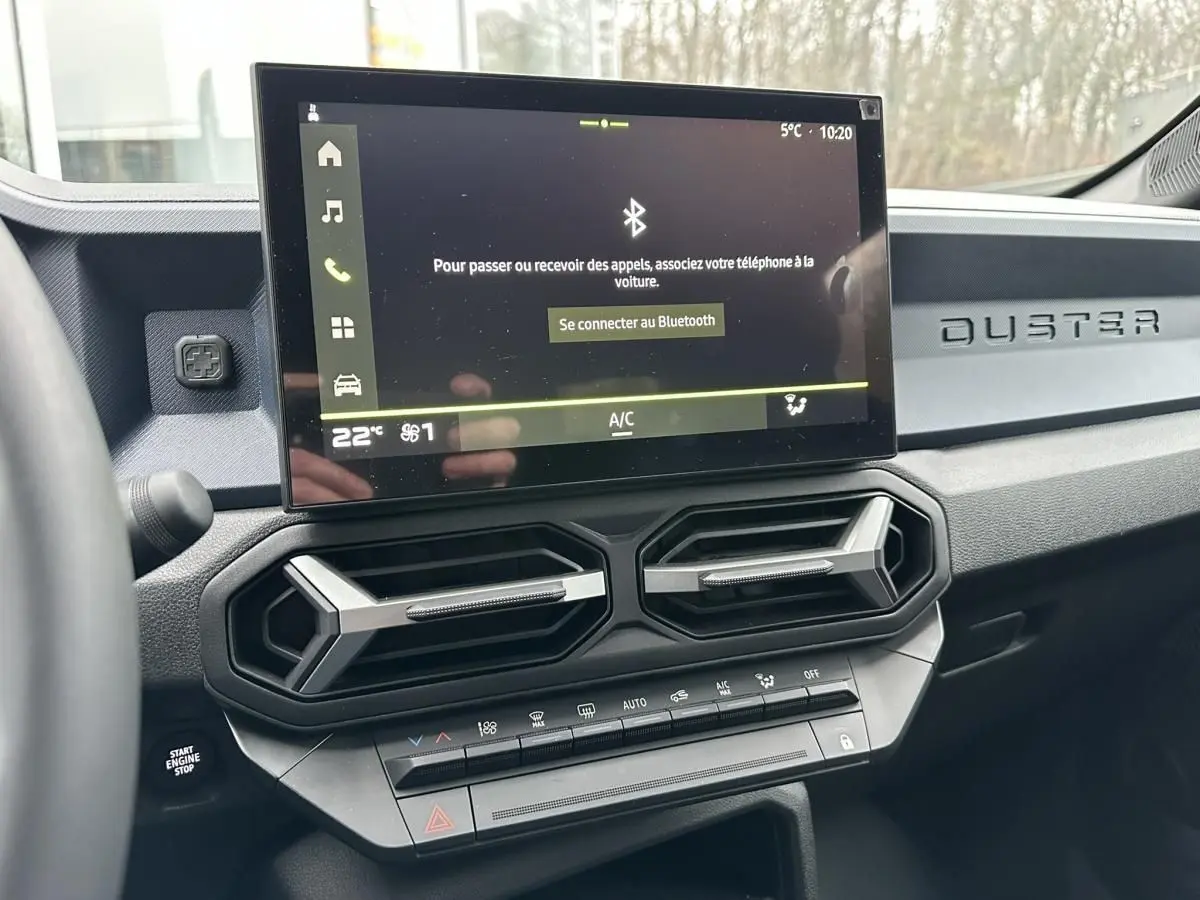 Vue intérieure du tableau de bord du Dacia Duster 2025 noir, avec écran tactile central et aérateurs hexagonaux.