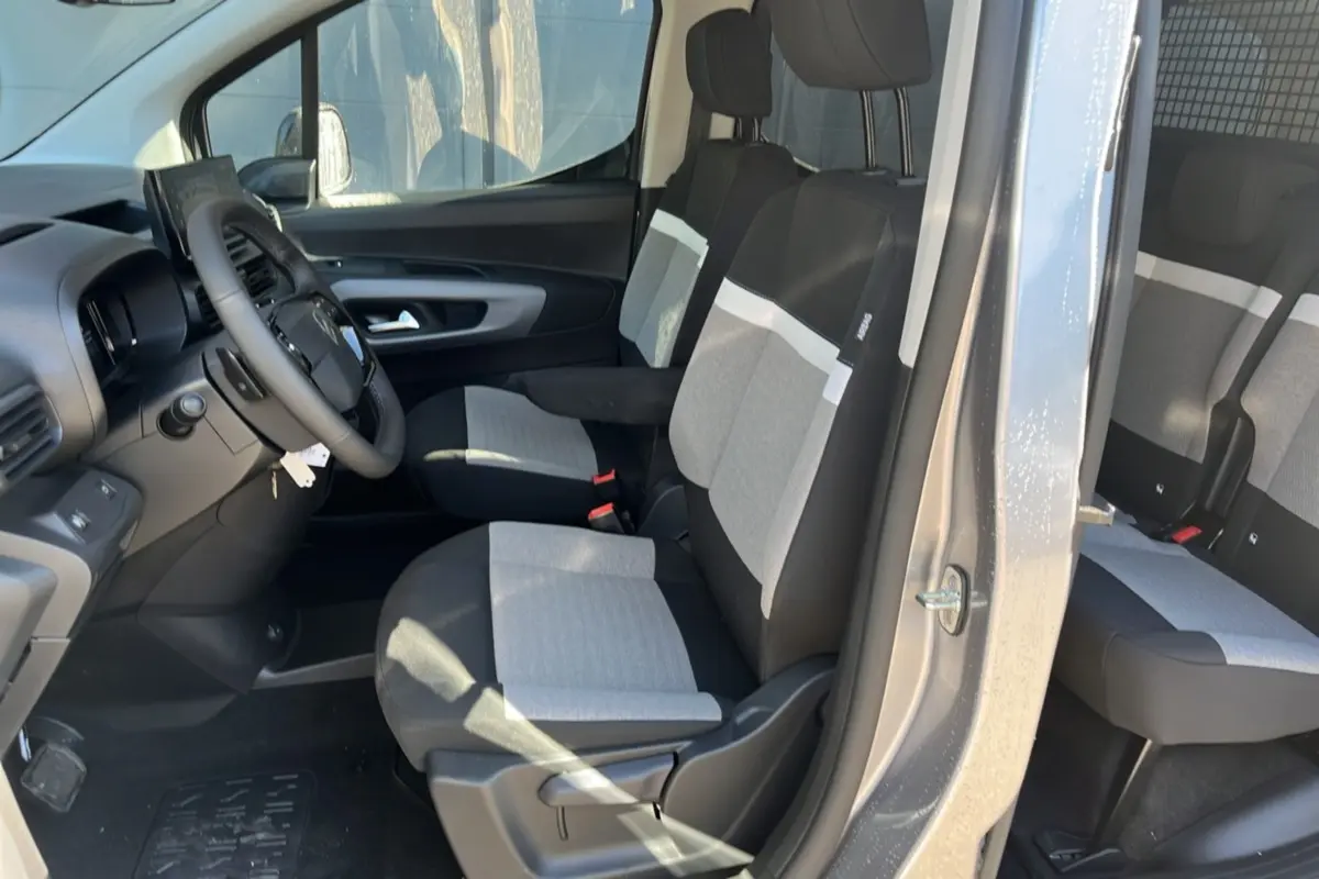 Vue intérieure côté conducteur du Citroën Berlingo gris Artense, mettant en valeur les sièges tissu bicolores et le volant cuir multifonctions.