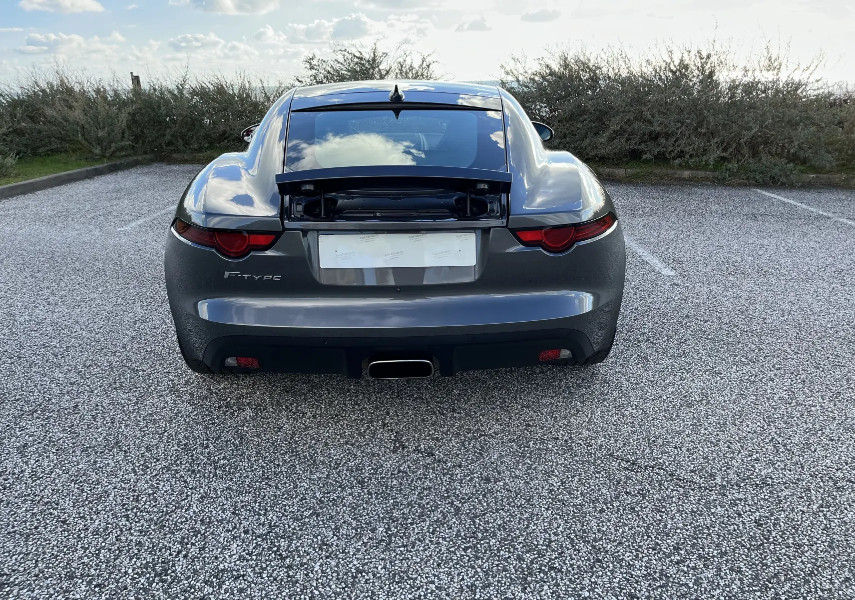 Vue arrière d'une Jaguar F-TYPE II Coupé 2.0T gris Corris avec coffre arrière ouvert et échappement central chromé.