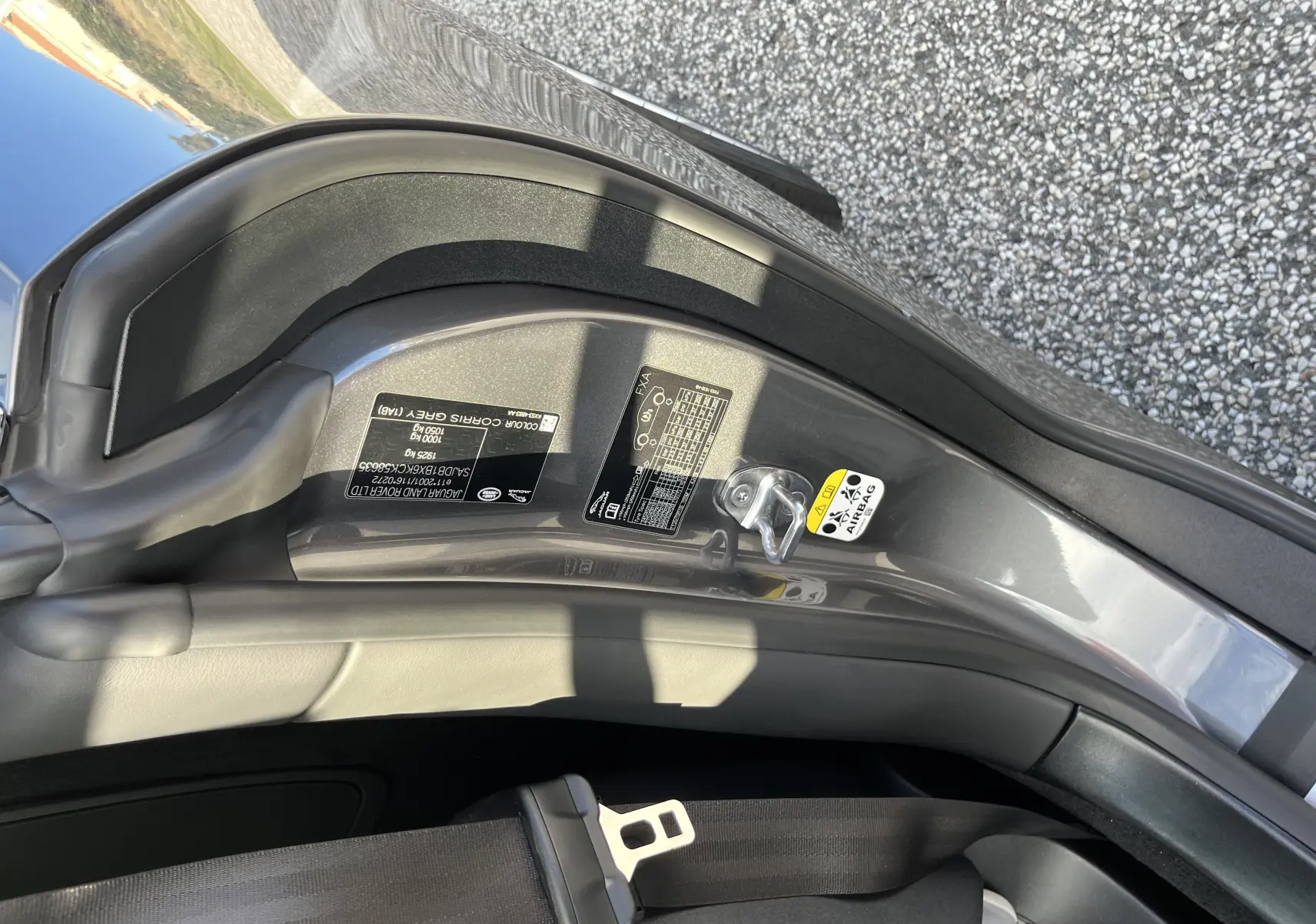 Détail de l'encadrement de porte côté gauche d'une Jaguar F-TYPE II Coupé gris Corris, avec étiquette d'information et ceinture de sécurité visible.