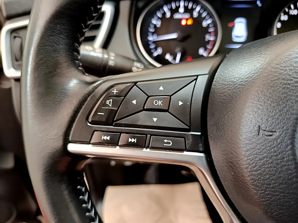 Gros plan sur les commandes multifonctions noires à gauche du volant cuir d’un Nissan Qashqai blanc 2019.