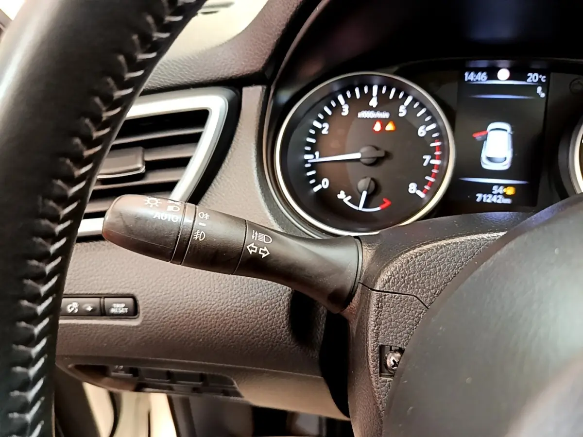 Gros plan sur le commodo gauche du tableau de bord noir du Nissan Qashqai blanc, avec compte-tours et écran multifonction.