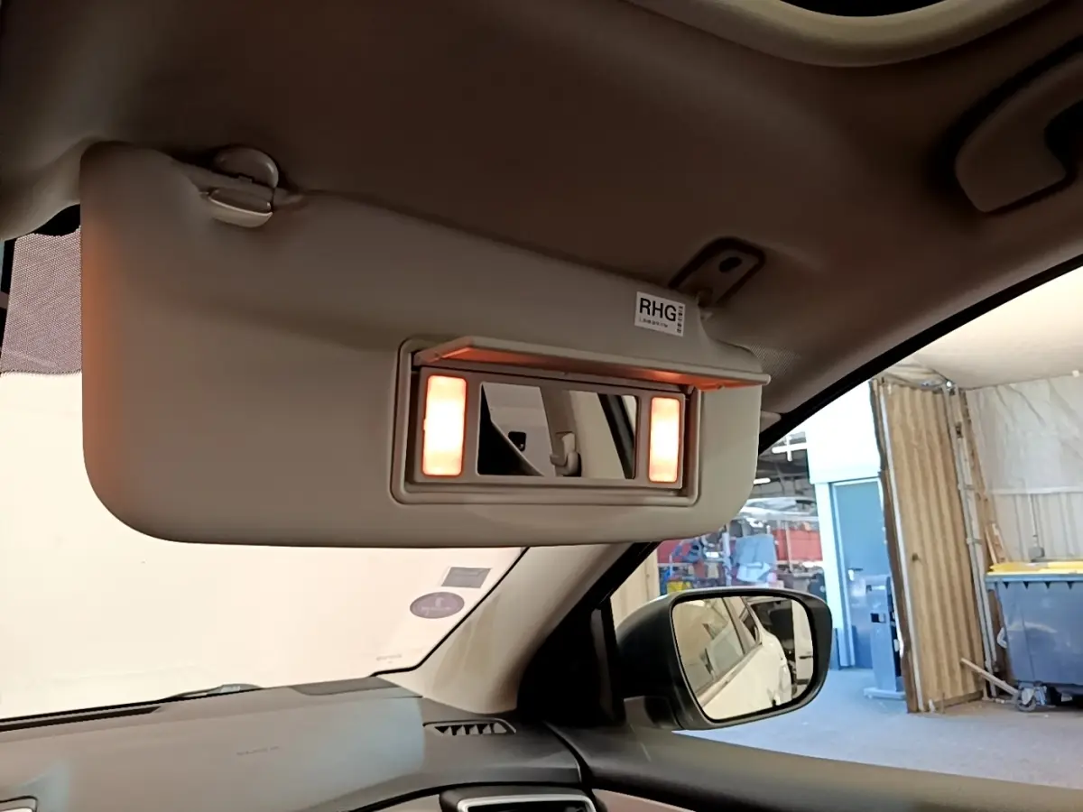 Détail de l'intérieur côté conducteur du Nissan Qashqai blanc 2019, miroir de pare-soleil éclairé avec rétro extérieur visible.