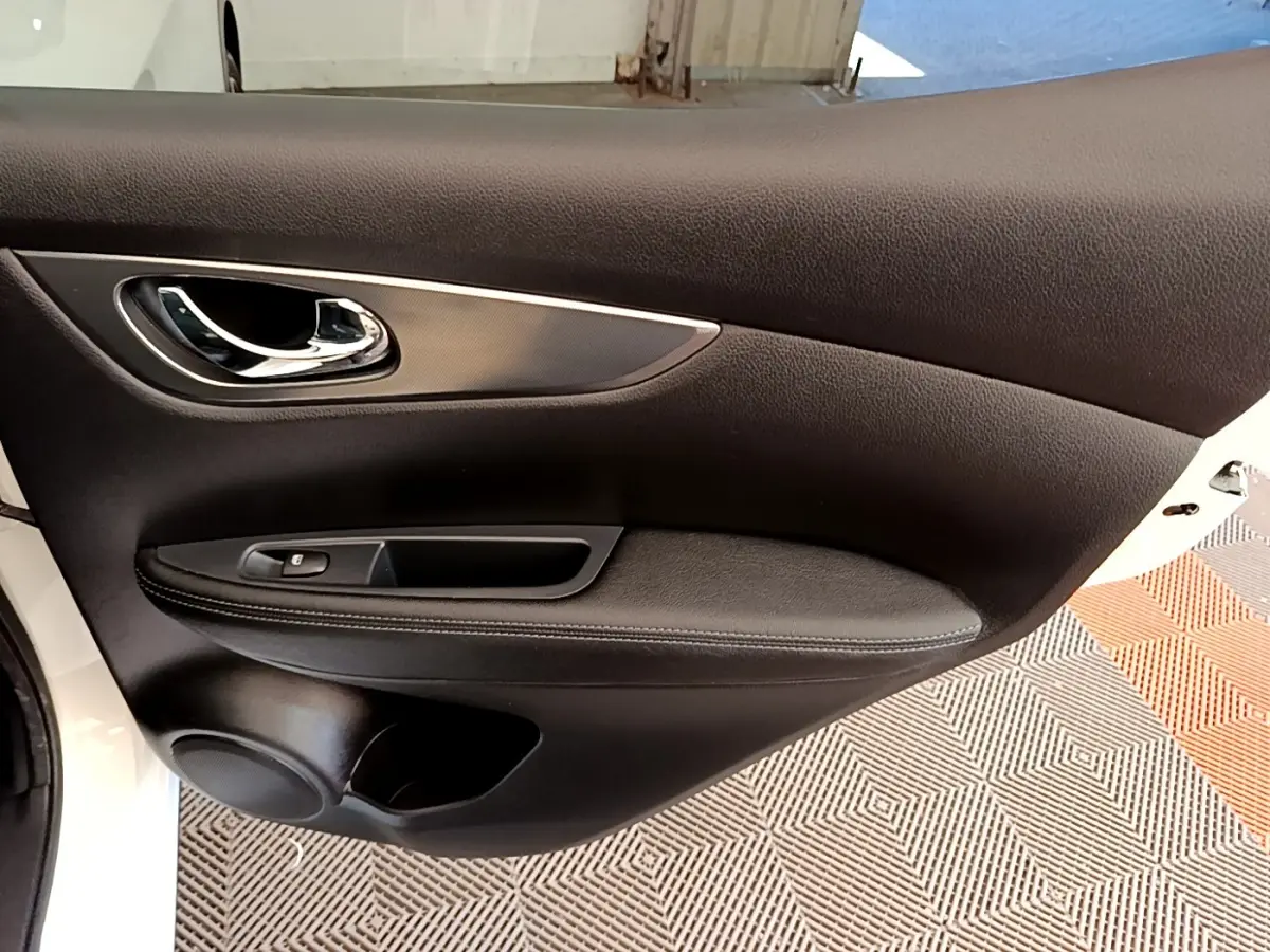 Gros plan sur la porte intérieure côté gauche du Nissan Qashqai blanc, avec poignée chrome et commande de vitre.