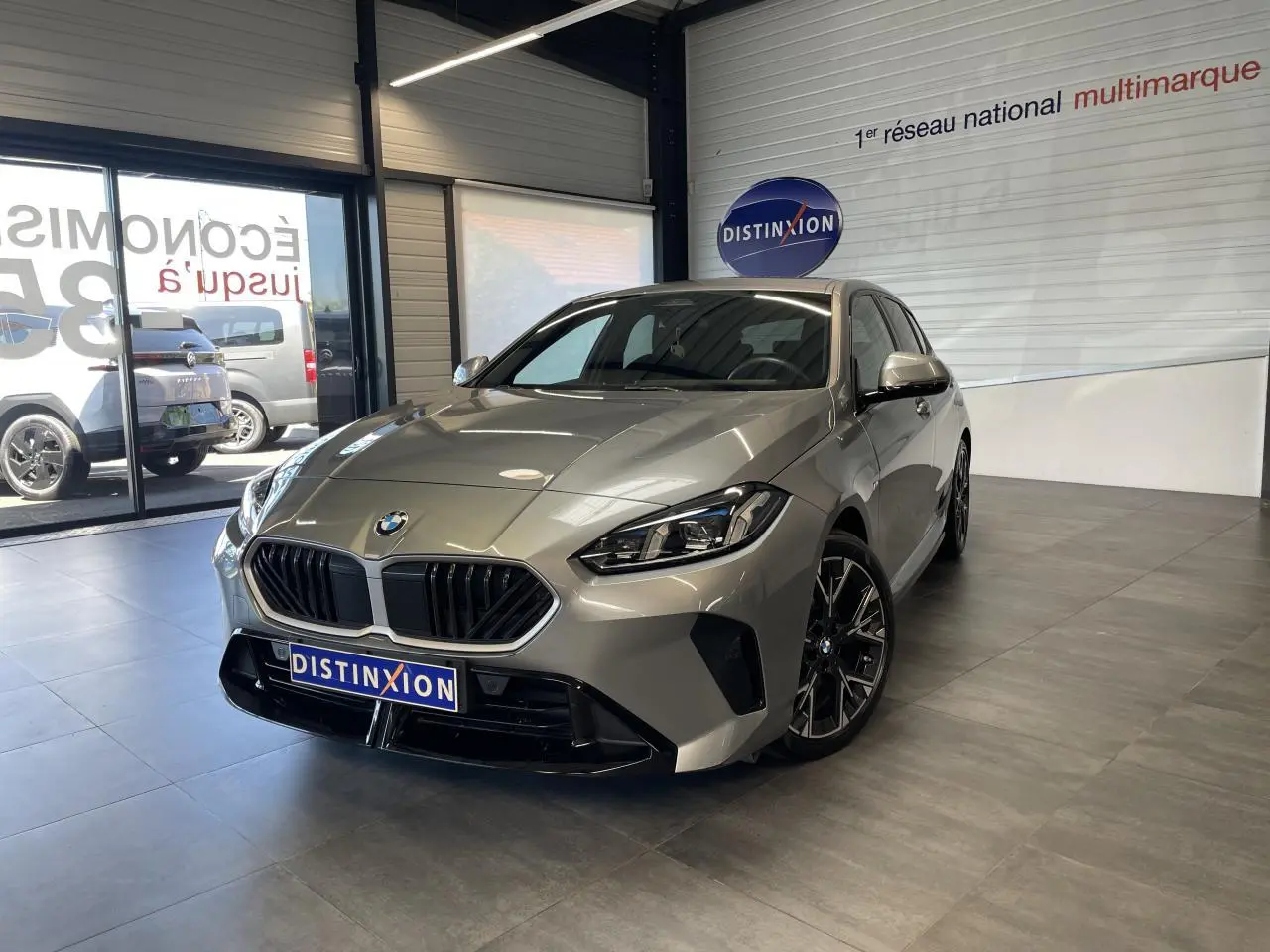 BMW Série 1 120d M Sport gris vue 3/4 avant en intérieur, avec calandre noire et jantes sport noires.