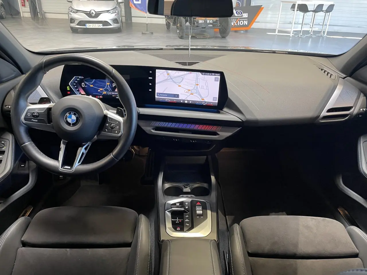 Vue intérieure avant de la BMW Série 1 120d M Sport 2025, tableau de bord moderne avec écran tactile et volant multifonction noir.