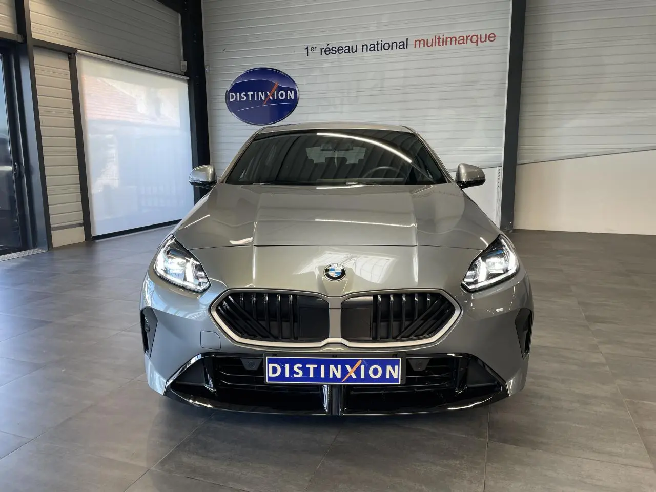 Vue frontale d'une BMW Série 1 120d M Sport gris métallisé avec calandre noire et phares allumés en showroom.