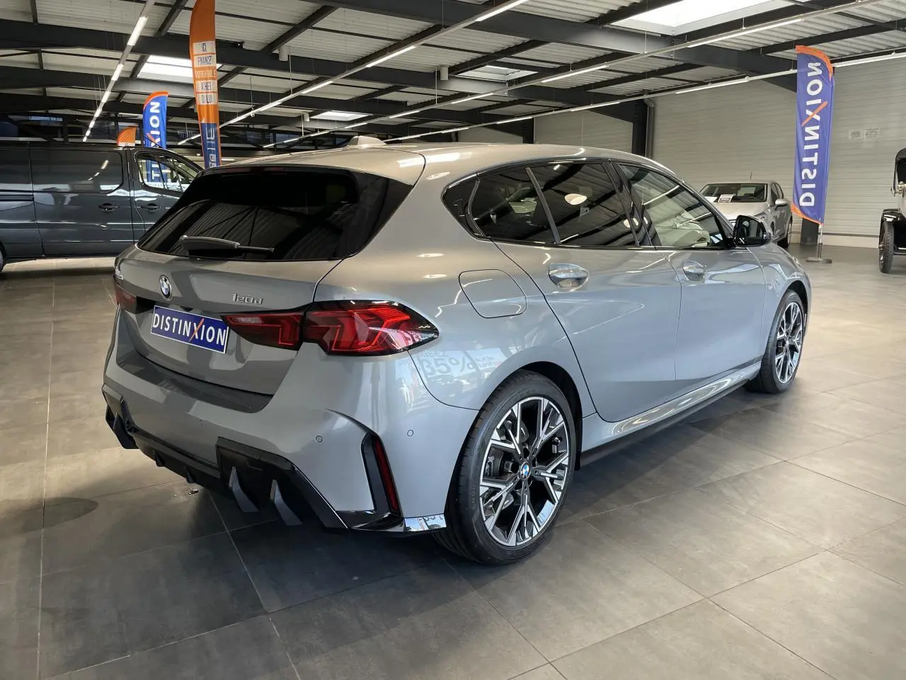 BMW Série 1 120d M Sport gris vue 3/4 arrière droit en intérieur avec jantes alliage et vitres teintées.