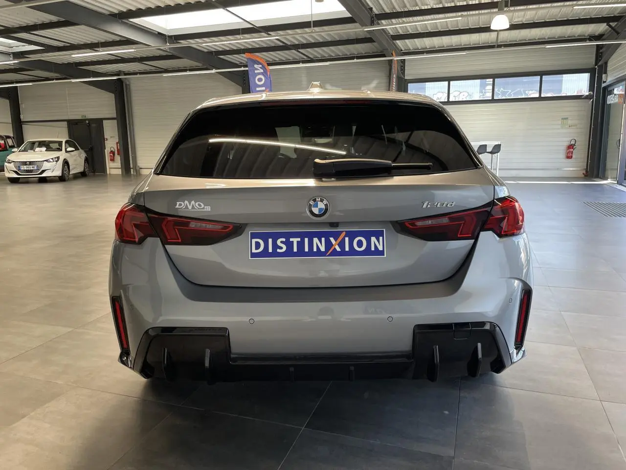 Vue arrière d'une BMW Série 1 120d gris 2025 en finition M Sport avec diffuseur noir et feux LED distinctifs.