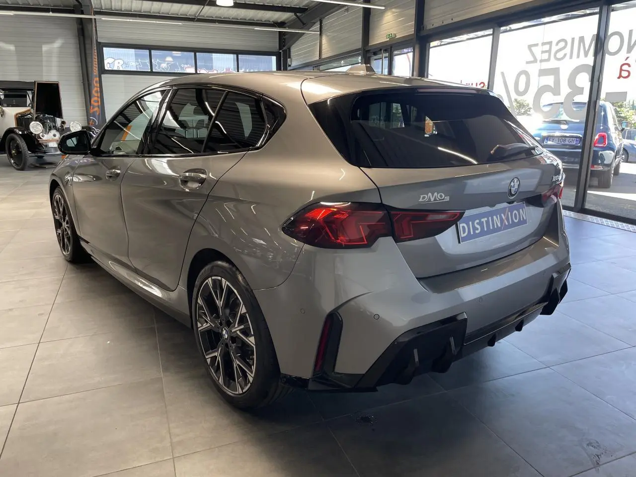 BMW Série 1 120d M Sport gris vue 3/4 arrière droit en intérieur, avec jantes sport et feux arrière LED distinctifs.