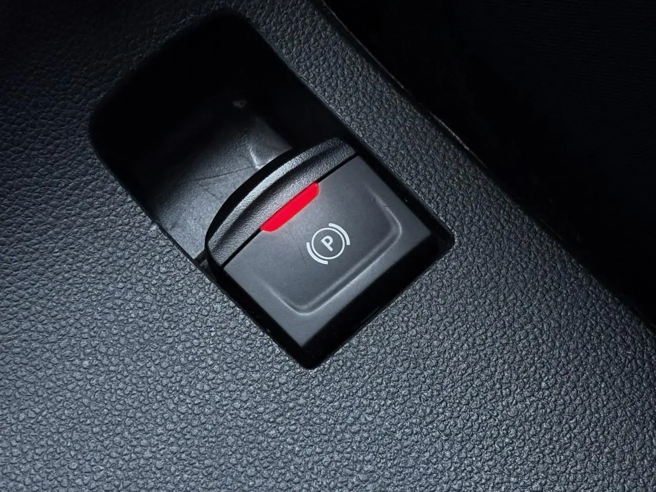 Gros plan sur le bouton de frein de parking électrique avec témoin rouge dans l'habitacle noir du Dacia Sandero Stepway 2025.