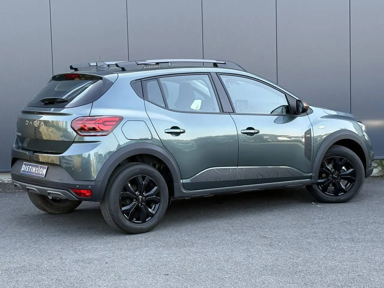 Vue latérale droite d'une Dacia Sandero Stepway 2025 Vert Cèdre avec jantes noires et barres de toit gris Mégalithe.