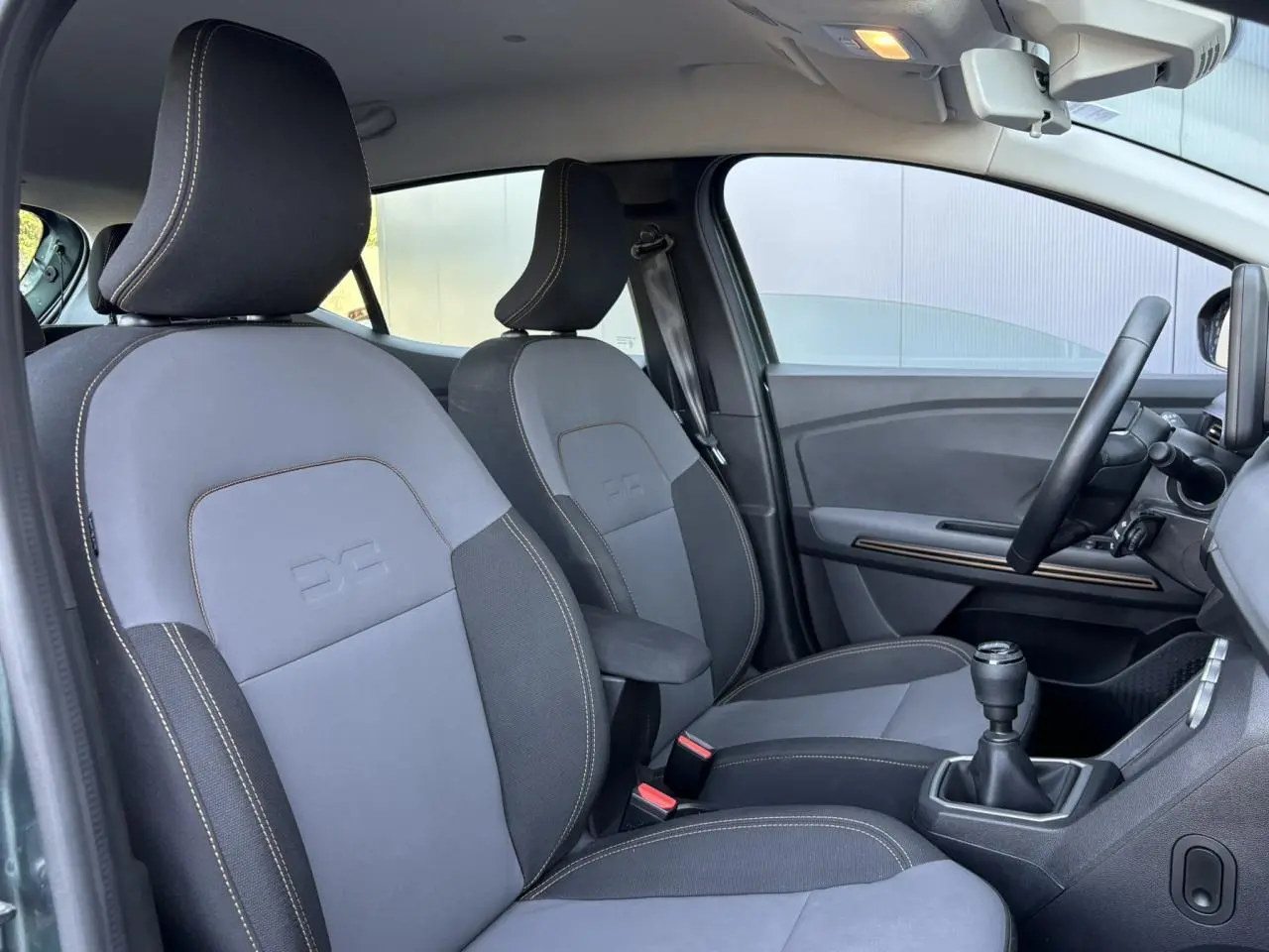 Vue intérieure côté conducteur de la Dacia Sandero Stepway 2025, sièges gris et noir avec accoudoir central.