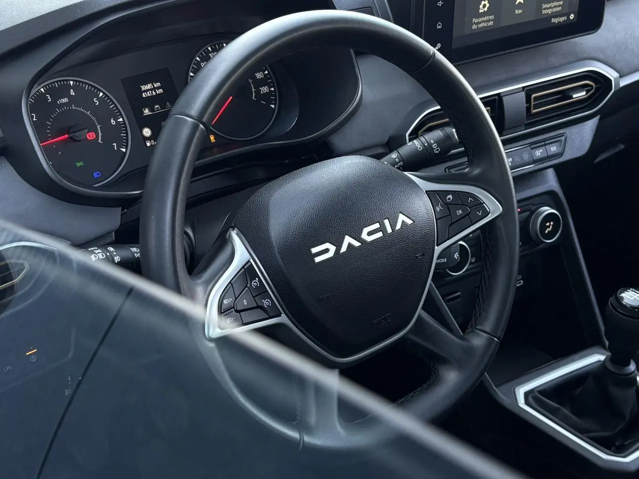 Vue rapprochée du volant noir Dacia et du tableau de bord avec écran tactile sur la console centrale d'une Sandero Stepway 2025.