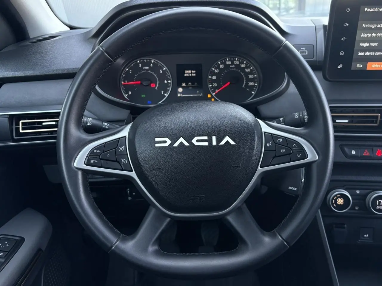 Vue rapprochée du volant noir de la Dacia Sandero Stepway 2025 avec commandes intégrées et tableau de bord numérique.
