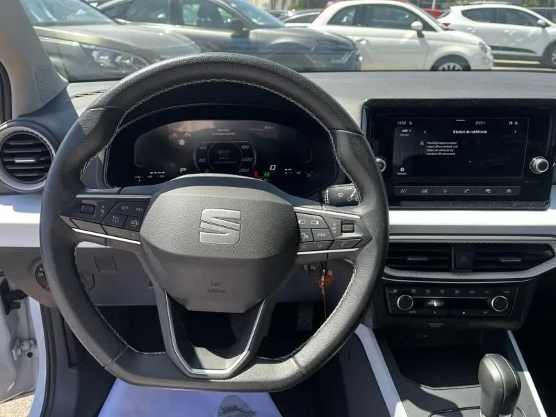 Vue intérieure centrée sur le volant noir du SEAT Arona blanc 2024 avec tableau de bord digital et écran tactile.