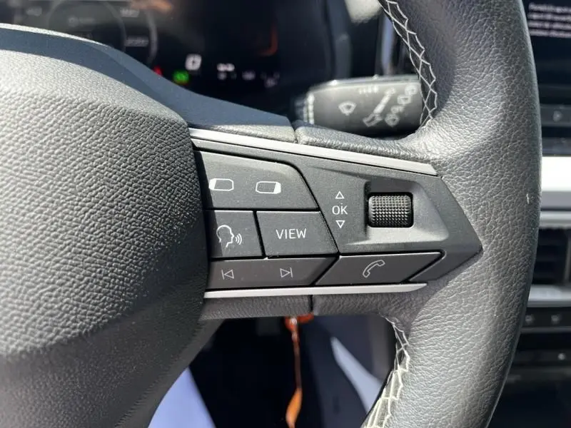 Gros plan sur les commandes multifonctions du volant en cuir noir du SEAT Arona blanc 2024, version 1.0 TSI 115 COPA DSG7.