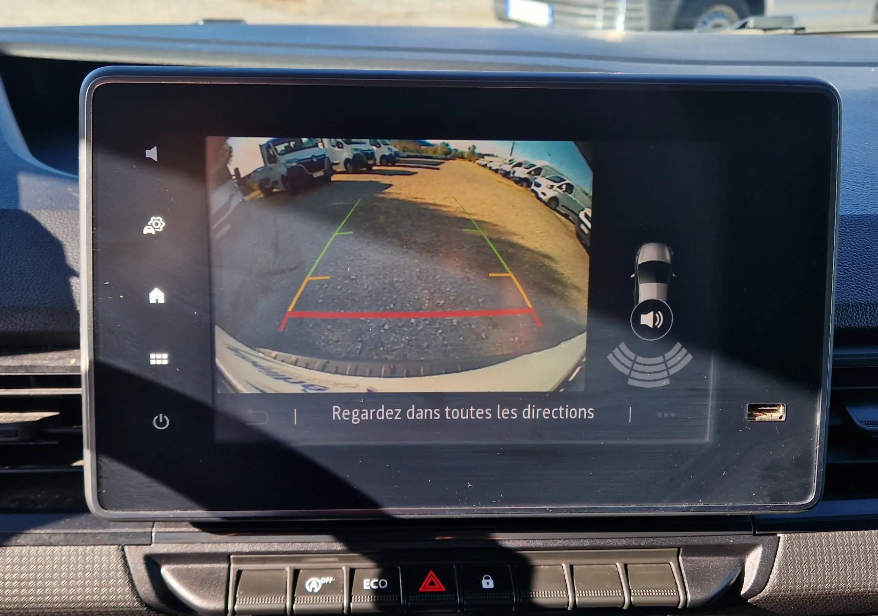 Écran intérieur montrant la caméra de recul du Renault Kangoo blanc, avec les lignes de guidage colorées visibles.