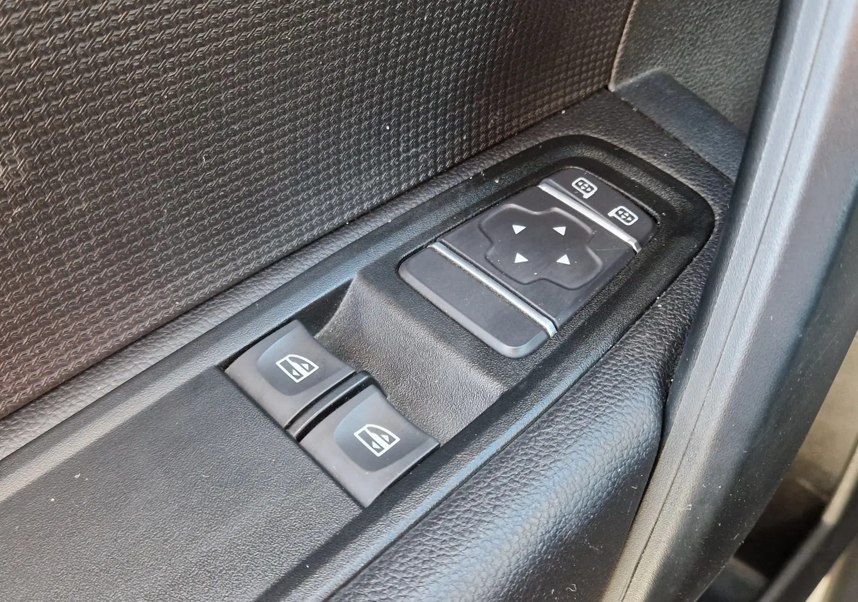 Gros plan sur les commandes de lève-vitres et réglage des rétroviseurs noirs dans une Renault Kangoo Van blanche 2023.