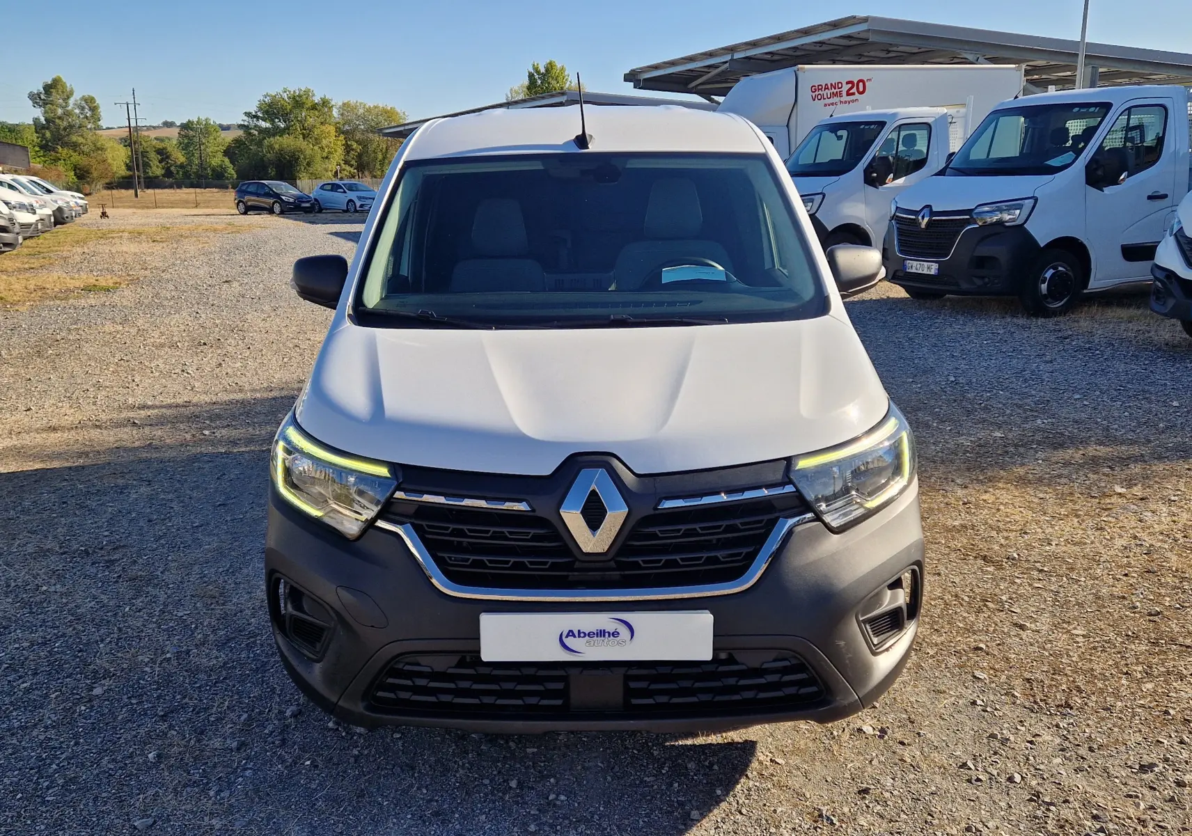 Vue de face d’un Renault Kangoo blanc 2023 avec calandre noire et phares allumés sur un parking extérieur.