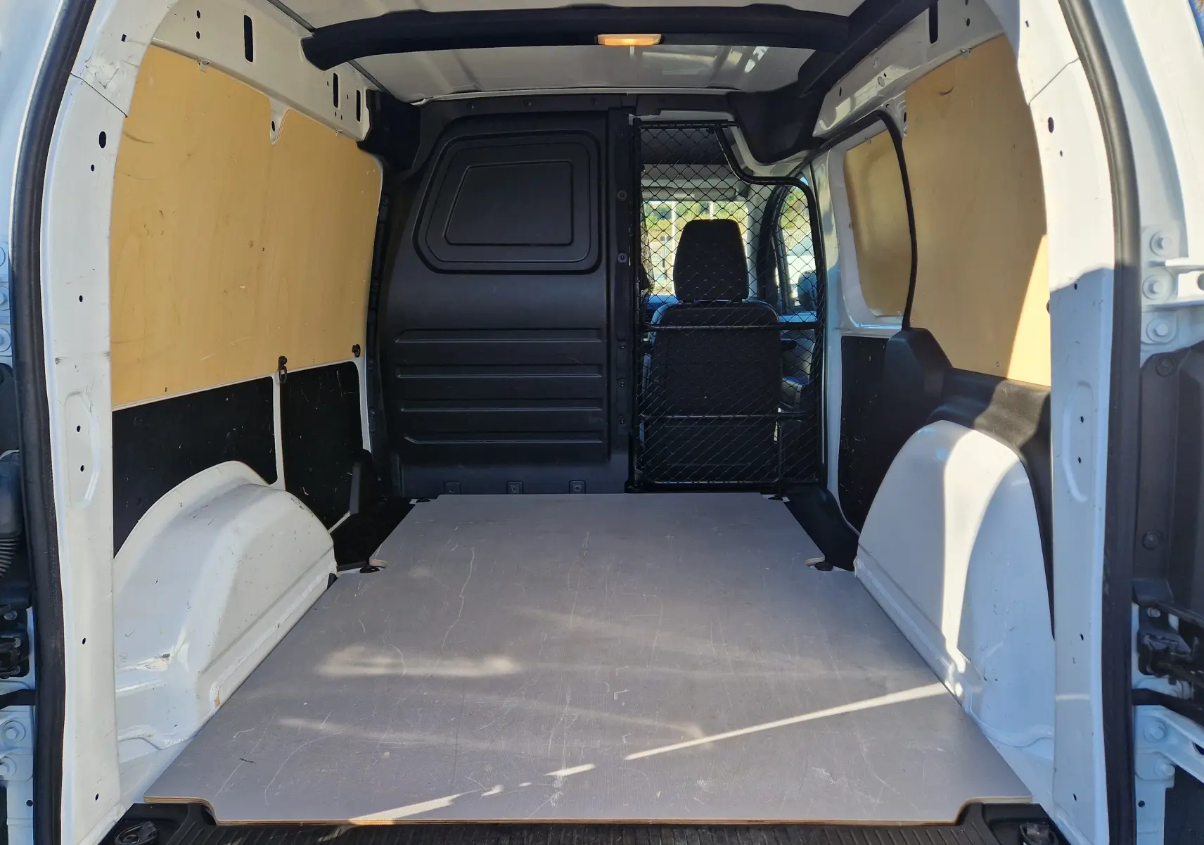 Vue intérieure arrière du Renault Kangoo Van blanc 2023, avec plancher plat, parois boisées et grille de séparation noire.