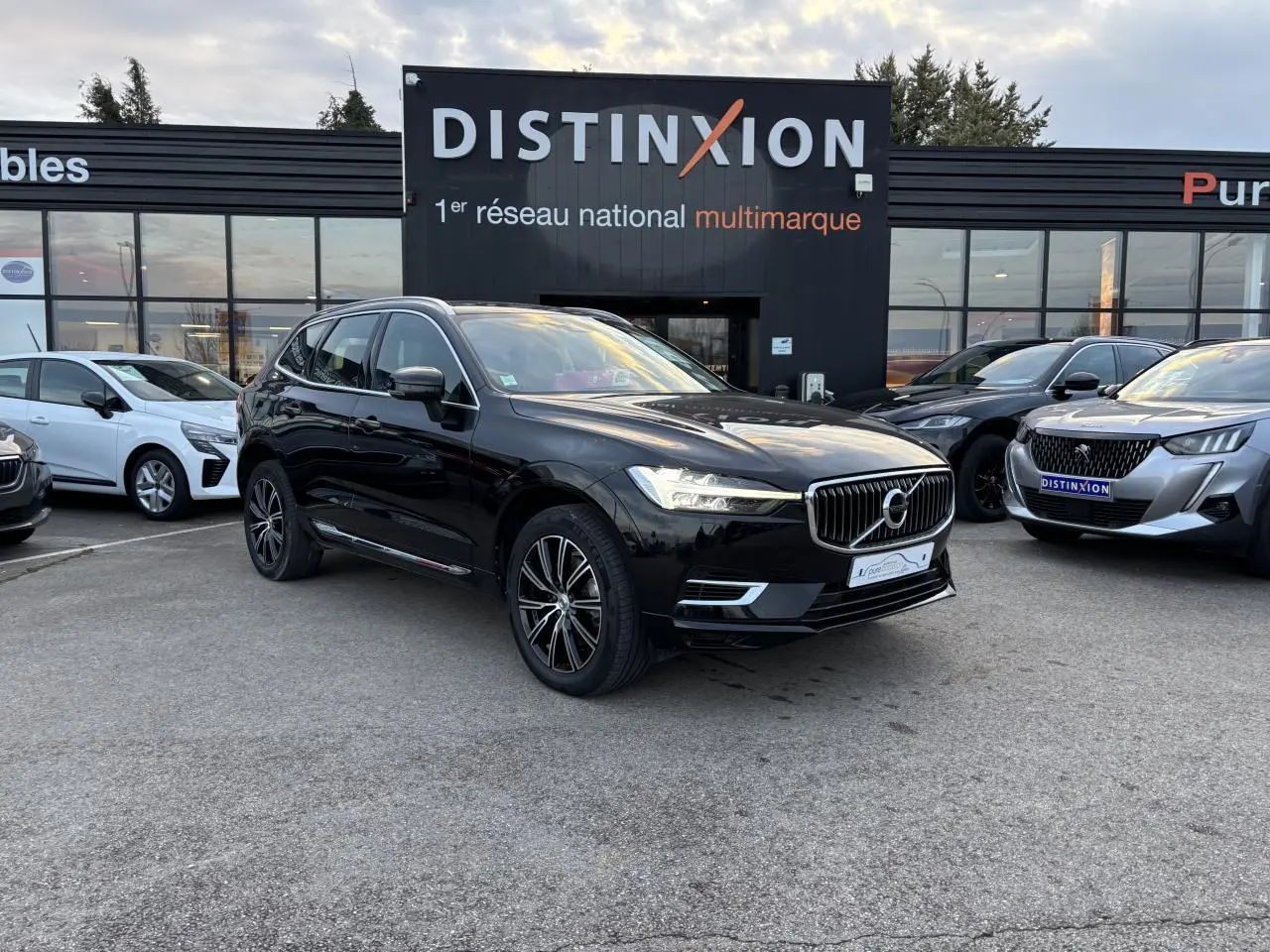 Volvo XC60 noir vue 3/4 avant droit sur parking devant concession multimarque Distinxion.