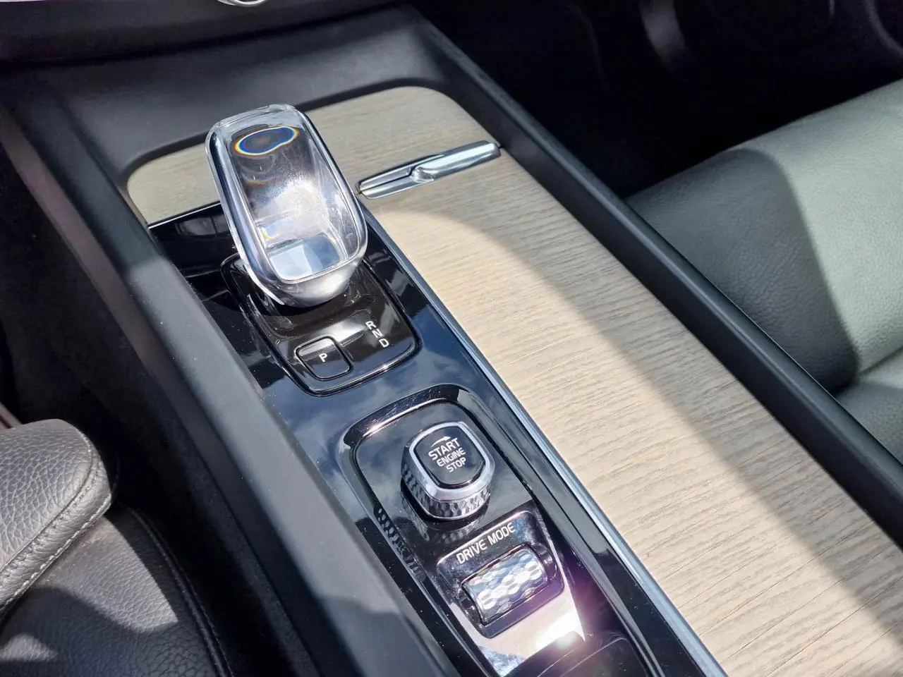 Gros plan sur la console centrale du Volvo XC60 noir, mettant en valeur le levier de vitesses en cristal et les commandes Start/Stop et Drive Mode.