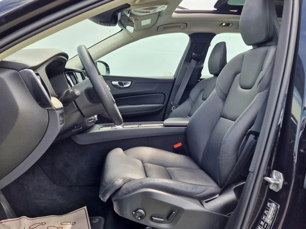 Intérieur côté conducteur du Volvo XC60 noir, sièges cuir confort avec réglages électriques et toit panoramique visible.