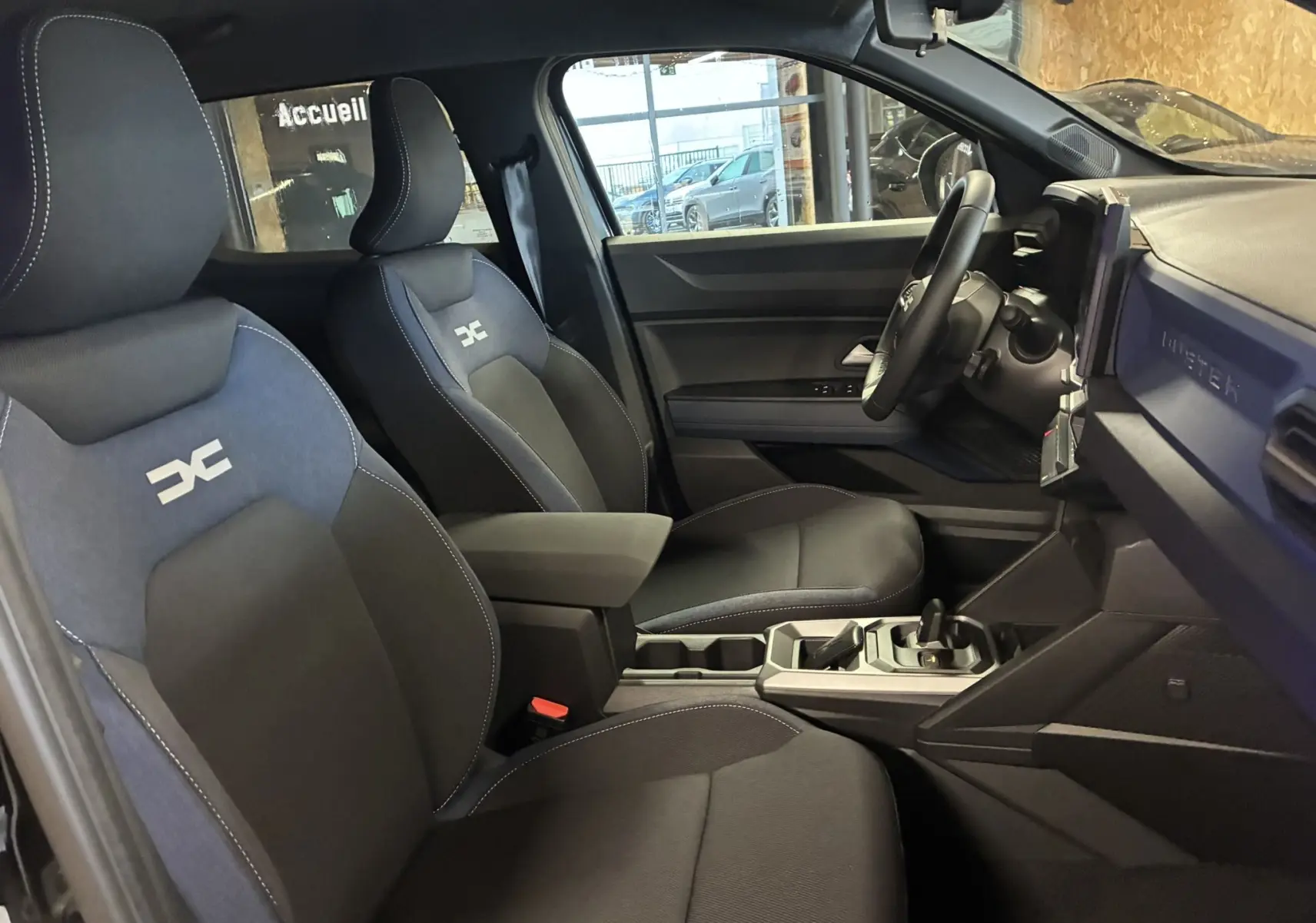Vue intérieure côté gauche du Dacia Duster 1.6 Hybrid 140 Journey 2025, sièges tissu noir et gris avec logo Dacia brodé.
