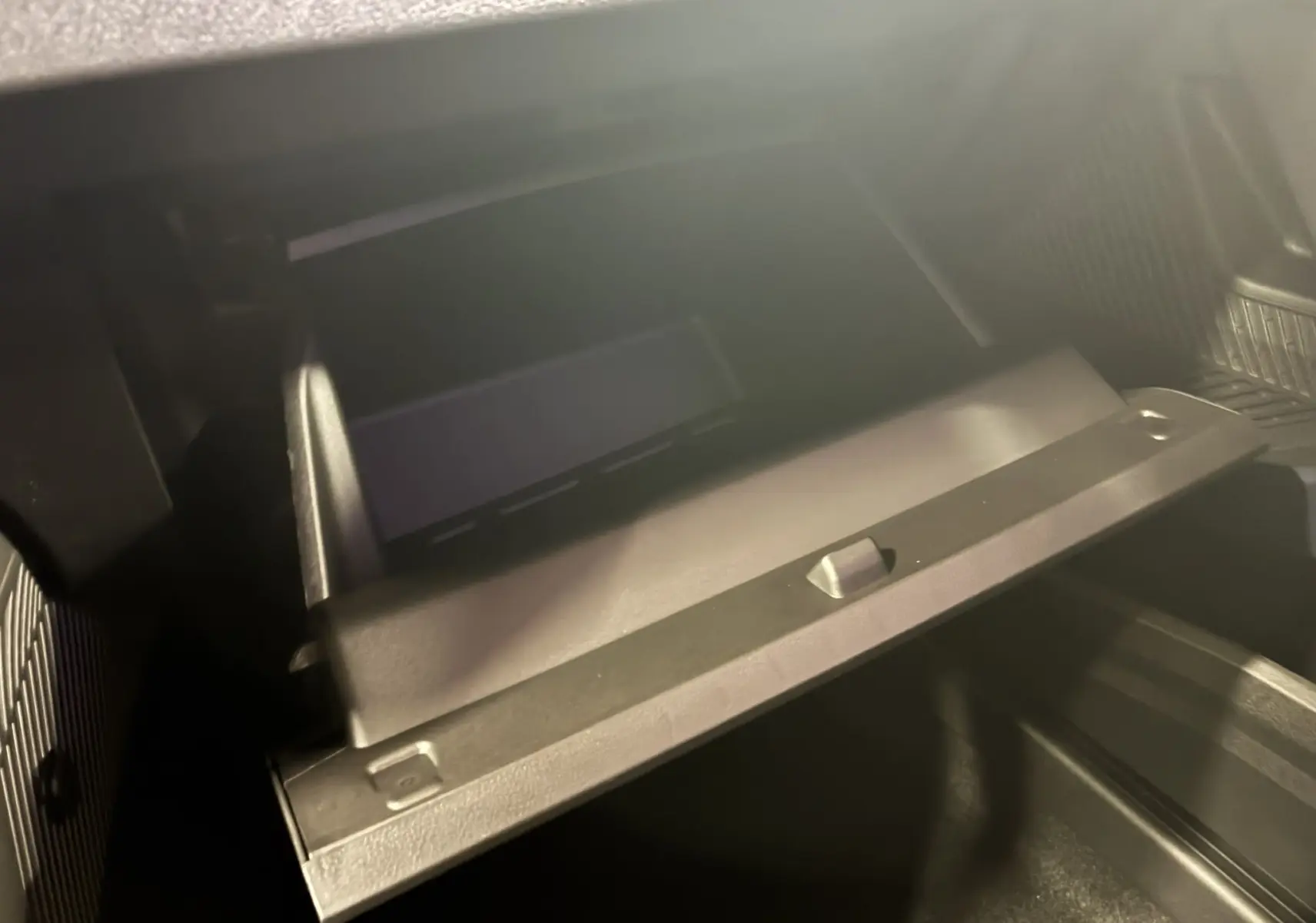 Gros plan sur la boîte à gants ouverte de la Dacia Duster 1.6 Hybrid 140 Journey noire, intérieur gris-noir en tissu.