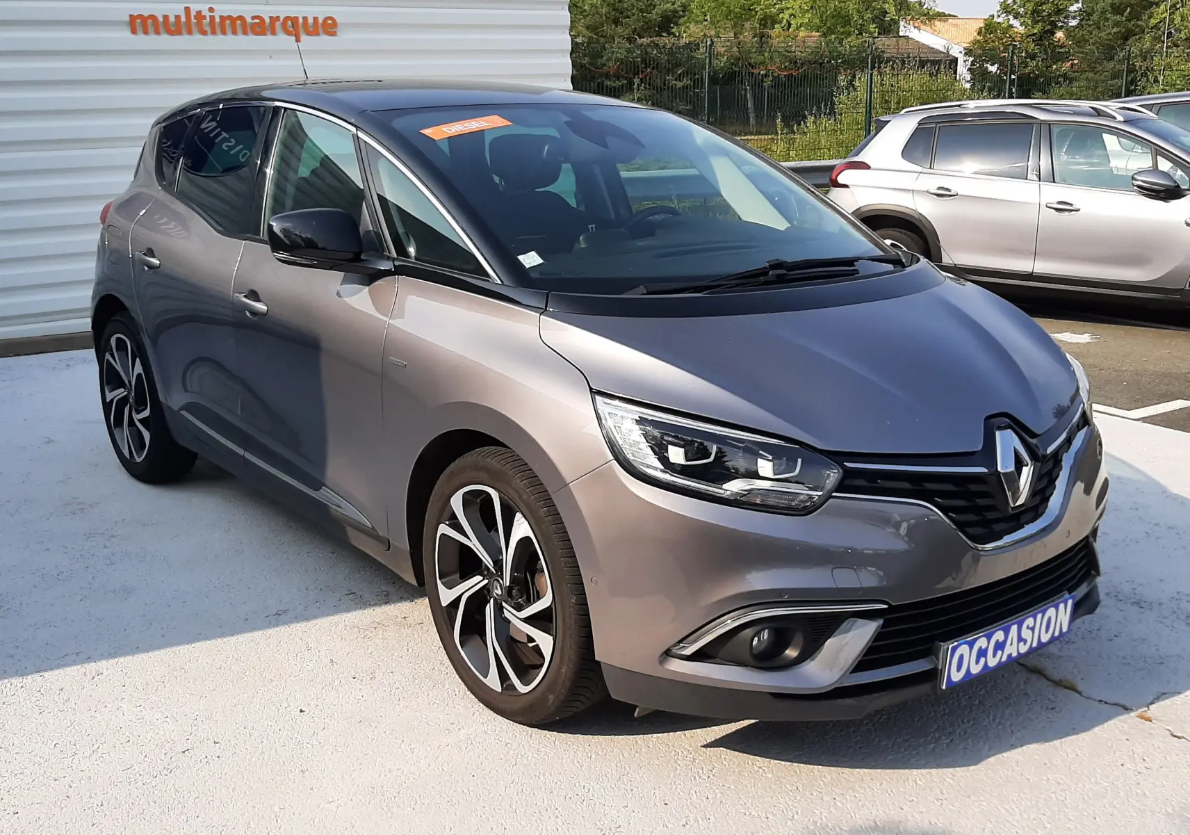 Renault Scénic IV gris Cassiopée avec toit noir, vue 3/4 avant, jantes alliage et calandre distinctive.
