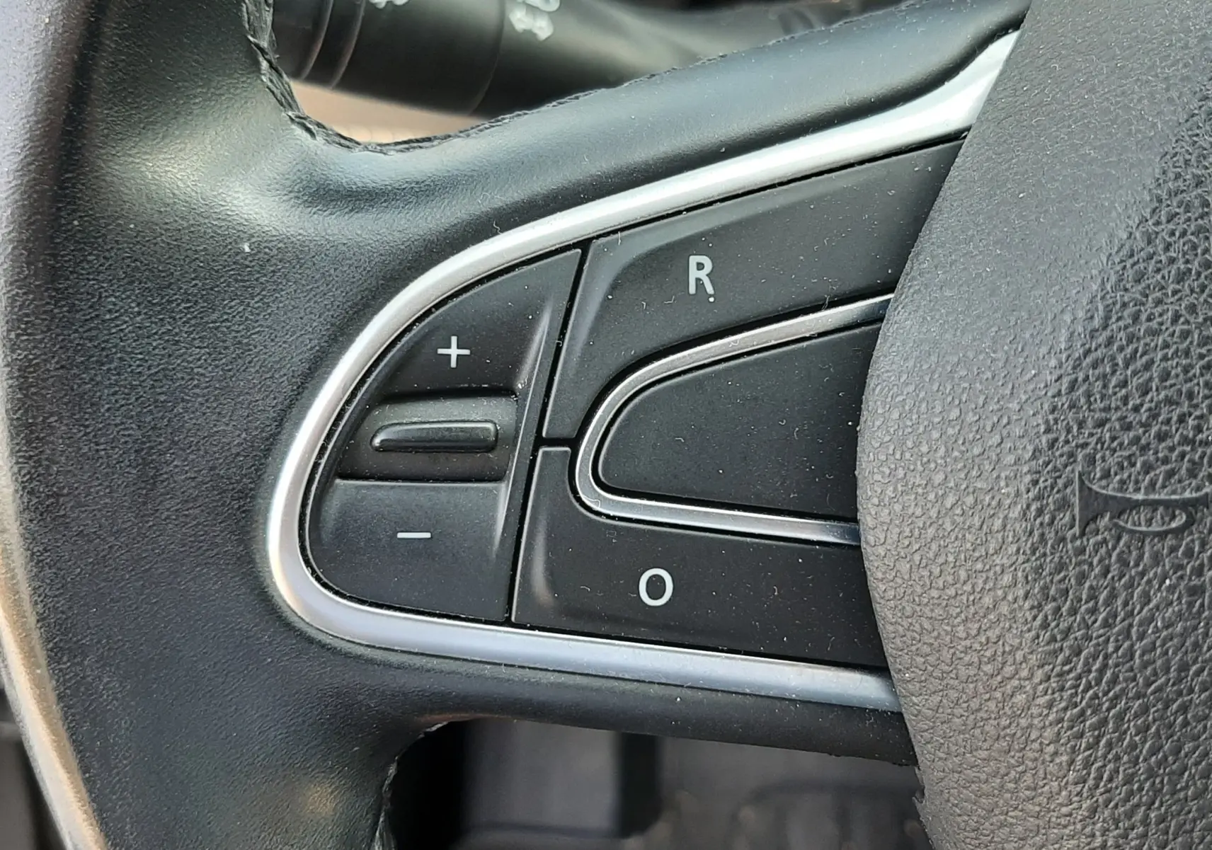 Gros plan sur les commandes gauche du volant noir du Renault Scénic IV gris Cassiopée, avec boutons de réglage et cruise control.