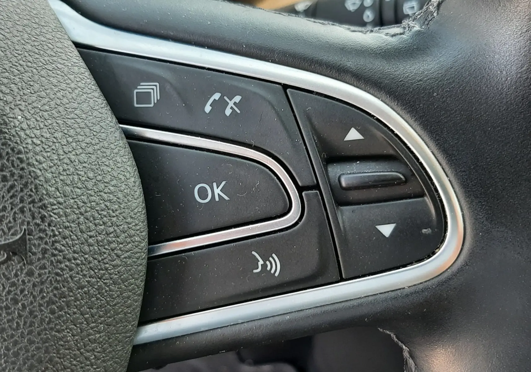 Gros plan sur les commandes multifonctions à gauche du volant en cuir noir du Renault Scénic IV gris Cassiopée.