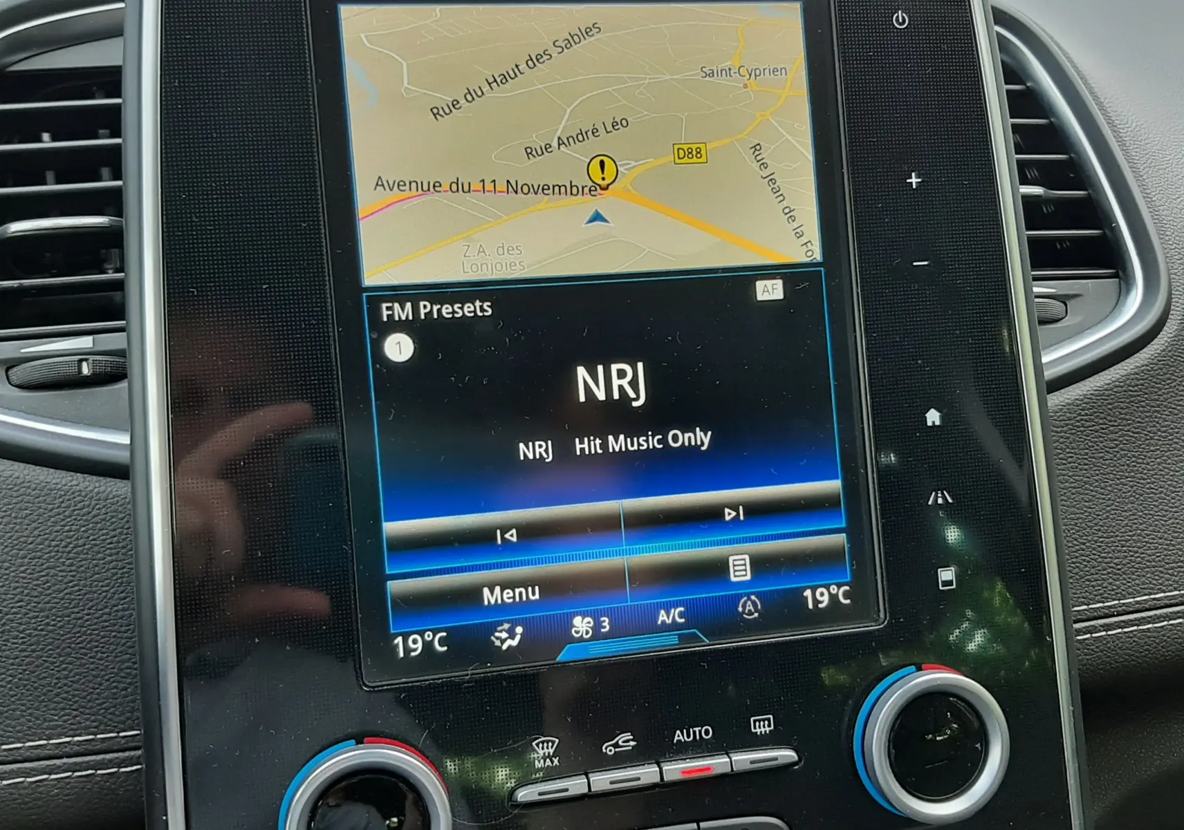 Vue rapprochée de l’écran tactile central du Renault Scénic IV gris cassiopée, affichant la navigation et la radio NRJ.