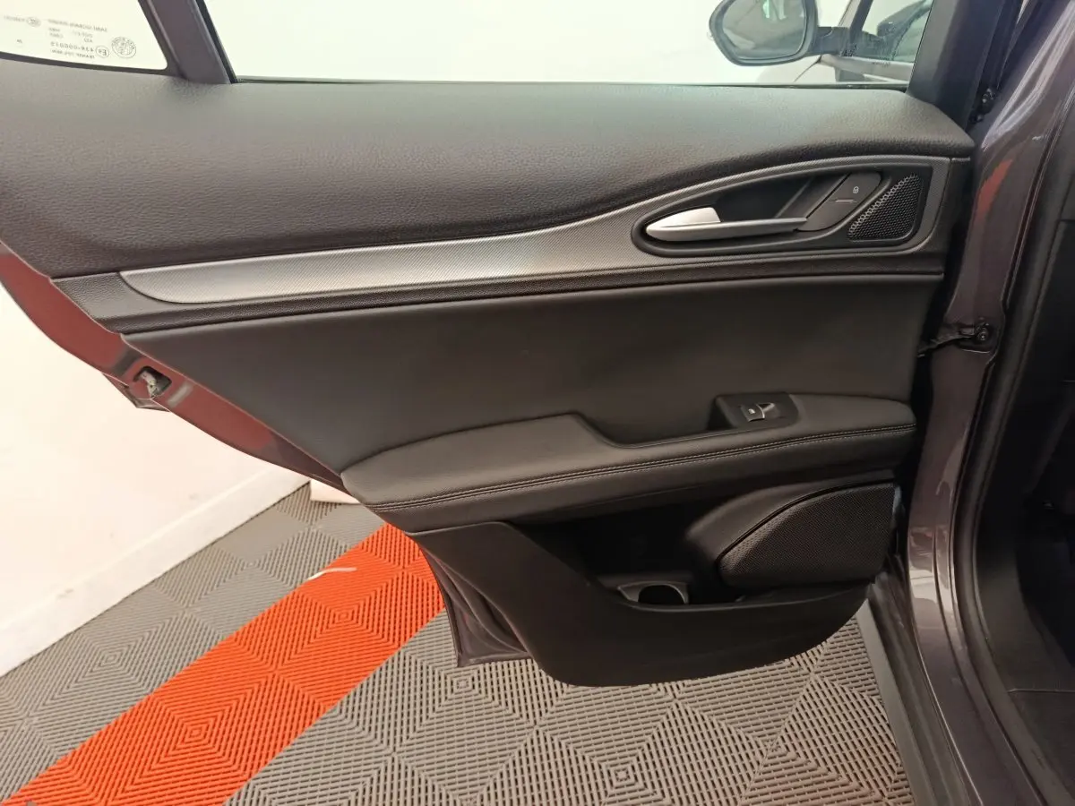 Porte côté gauche ouverte d'un Alfa Romeo Stelvio gris foncé, avec garniture noire et poignée alu intégrée.