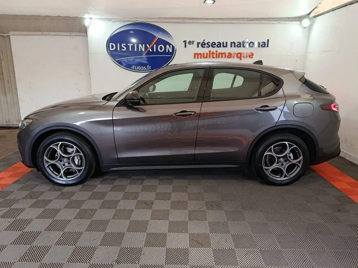 Profil côté gauche d'un Alfa Romeo Stelvio gris foncé 2024 Sprint, avec jantes distinctives et feux arrière LED allumés.