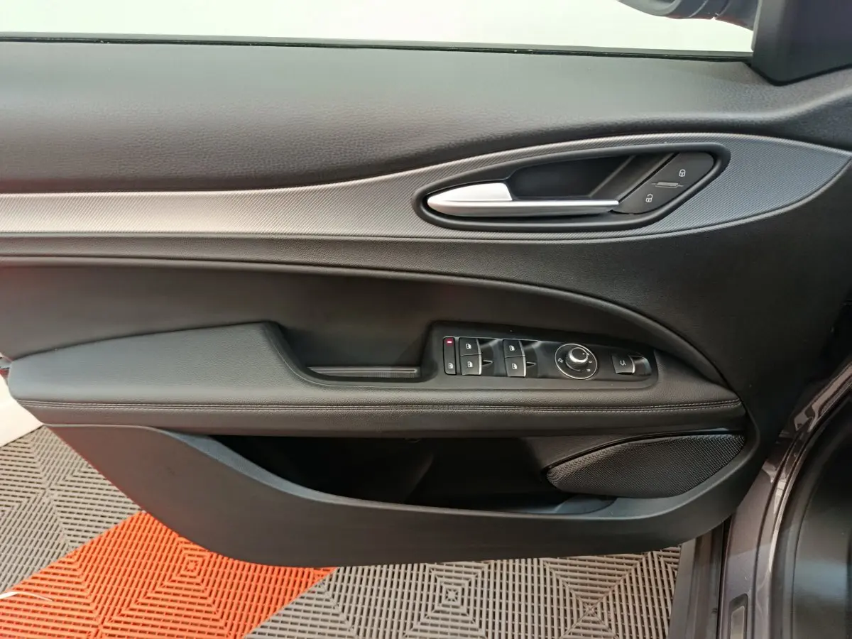 Gros plan sur la porte côté gauche de l'Alfa Romeo Stelvio gris foncé, avec commandes électriques et poignée argentée.