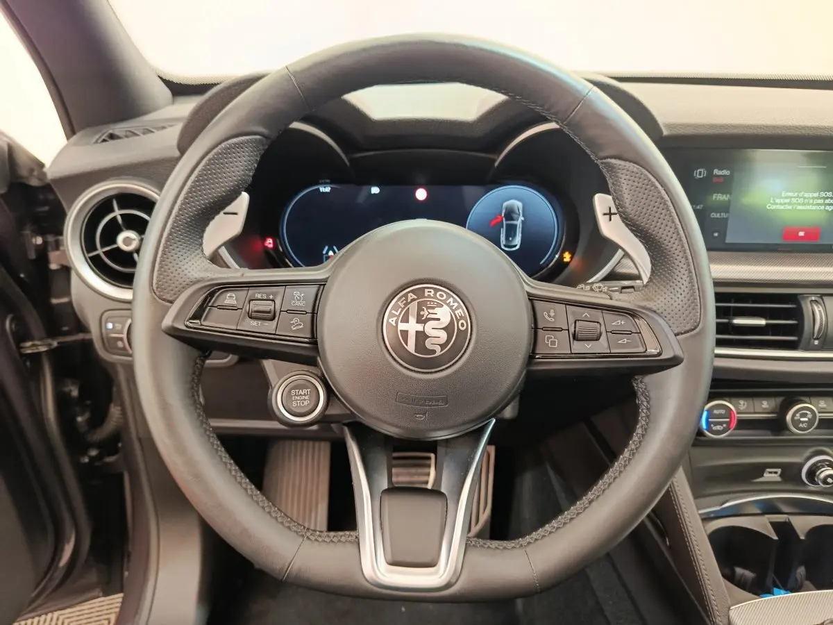 Vue rapprochée du volant cuir et aluminium de l'Alfa Romeo Stelvio 2024 avec tableau de bord numérique et commandes intégrées.