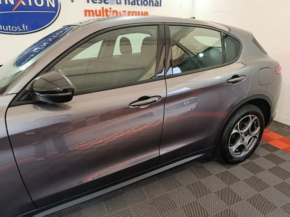 Profil côté gauche de l'Alfa Romeo Stelvio gris foncé 2024 avec jantes distinctives et rétroviseur noir brillant.